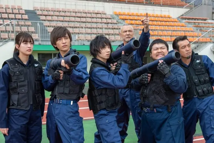 The SMAT stand in a stadium together in their uniforms, holding giant vinegar cannons.