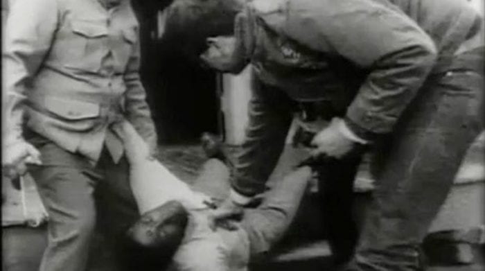 A group of men, baling hooks in hand, move Ben's dead body, bullet hole in his forehead clearly visible, out the door and down the porch steps.