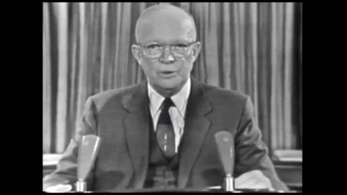 Dwight Eisenhower, in suit and tie, microphones in front of him, a curtain behind him, dressed in suit and tie and wearing glasses, gives his final speech as president.