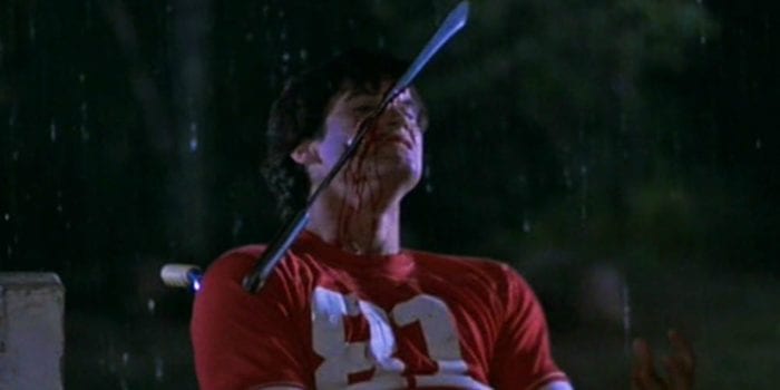 Mark, in a wheelchair, wearing a jersey emblazoned with the number 81, a machete lodged in his face, about to roll backwards down a flight of stairs in the rain.