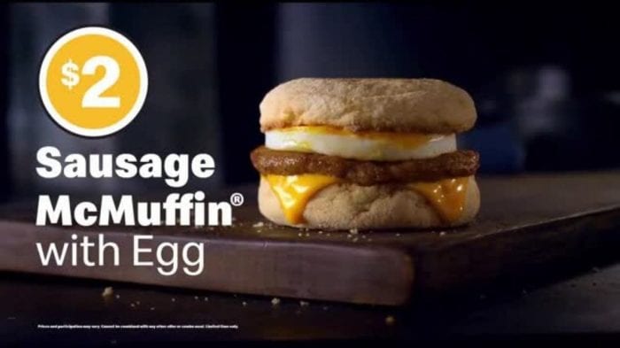 A sausage McMuffin: an English muffin sandwich with a circular sausage patty, fried egg, and slice of melted cheese. Next to it, the words: $2 and Sausage McMuffin with Egg.