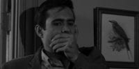 Norman Bates, hand over his mouth, standing against the door frame.