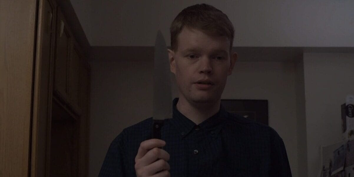 An expressionless man holds a knife