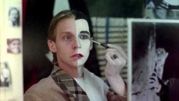 a young man sits and paints his face exactly down the middle. One half remains the image of the boy with sandy hair, the other half painted white with jet black hair resembling a vampire.
