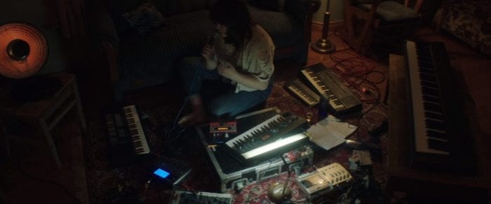 Catherine sits on the floor surrounded by various instruments, cords and electronic equipment.