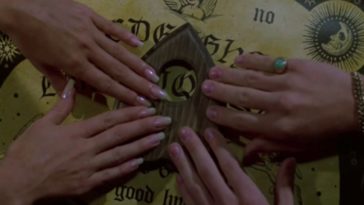 Four hands touching the planchette of a ouija board.