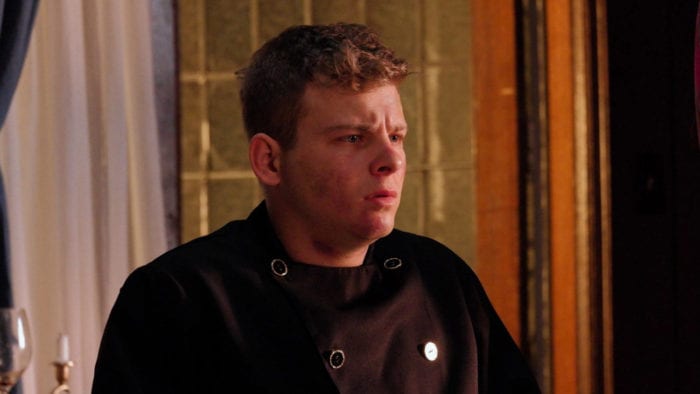 Sydney dons a black chef's uniform and looks a little shaken by what he sees off-camera right