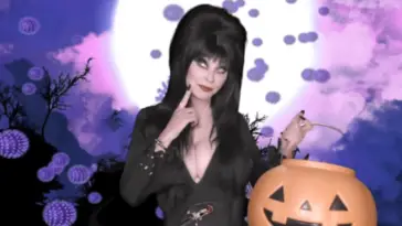 Elvira, Mistress of the Dark (Cassandra Peterson), looks thoughtful while holding a large jack-o-lantern trick-or-treat bucket.
