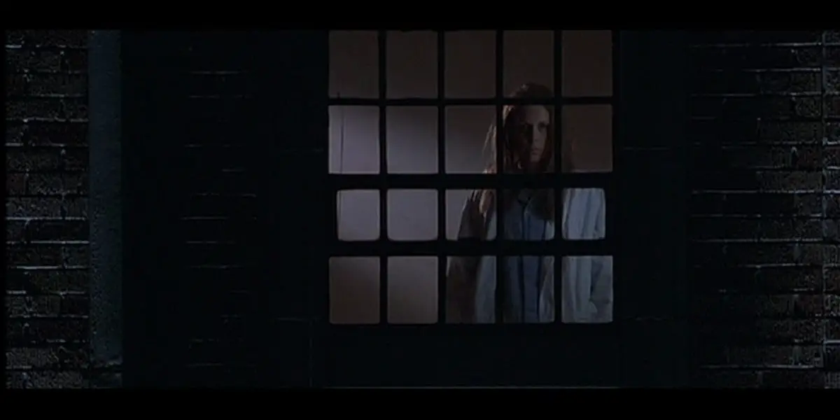 Jamie Lee Curtis looks out her window in the night while standing inside.