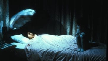 A person lays in bed with two horrifying figures surrounding them, haunting them.