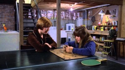 a mother and daughter sit at a ping pong table in a basement with a ouija board between them - still shot from the Exorcist