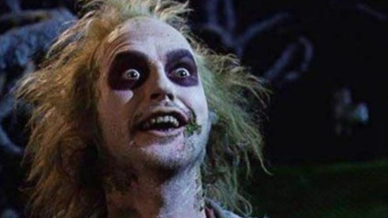 Close frame of Beetlejuice, with messy green hair, green mold on skin, and blackened eyes, looks excitedly into the camera.
