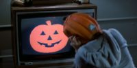 A kid watching TV in a pumpkin mask