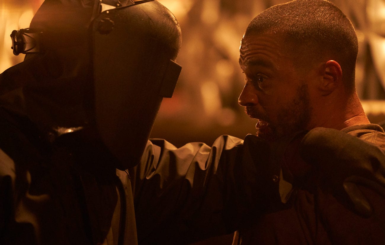 The Man, on the left left, wearing baggy black clothes, gloves, and a welding mask has his hand on the shoulder of a terrified Todd, on the right.