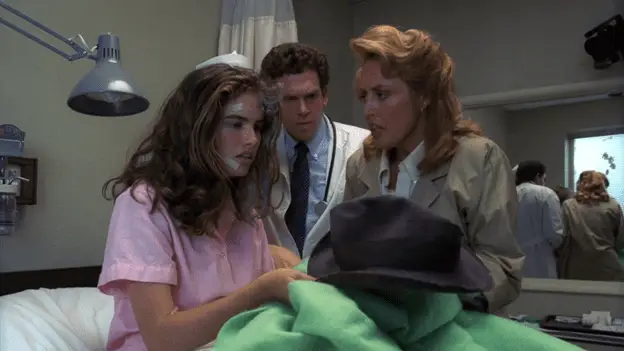 Nancy, in a nightgown, sits up in a hospital bed holding Fred Krueger's crumpled fedora in one hand, while her mother looks at her in concern and, behind her, the doctor looks incredulously at the hat.