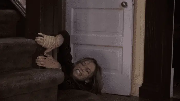 Beth grabs hold of the stairway banister and grits her teeth as she's pulled down into the basement
