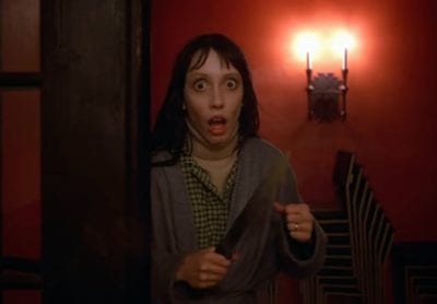 Shelley Duvall holds a knife and looks frightened with wide eyes and open mouth in The Shining.