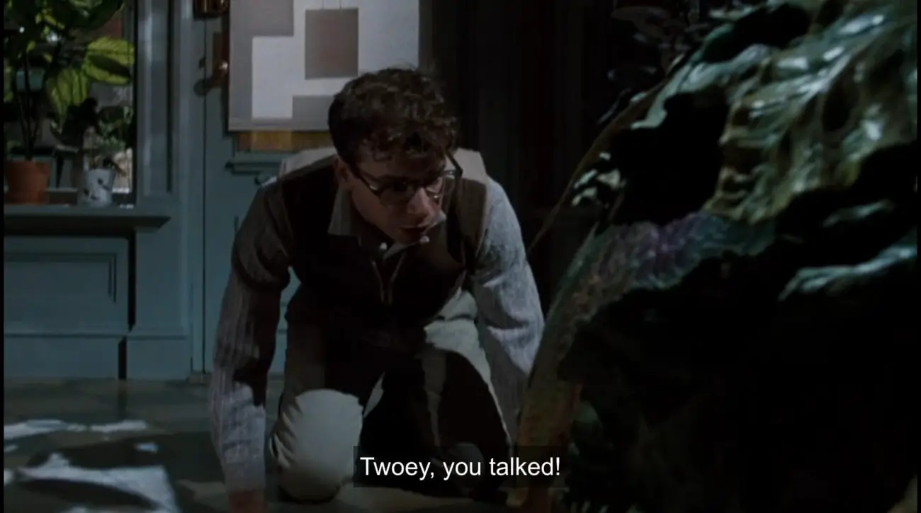 Seymour Krelborn (Rick Moranis) kneels in front of carnivorous plant Audrey II, exclaiming, "Twoey, you talked!", in the film, "Little Shop of Horrors" (1986).