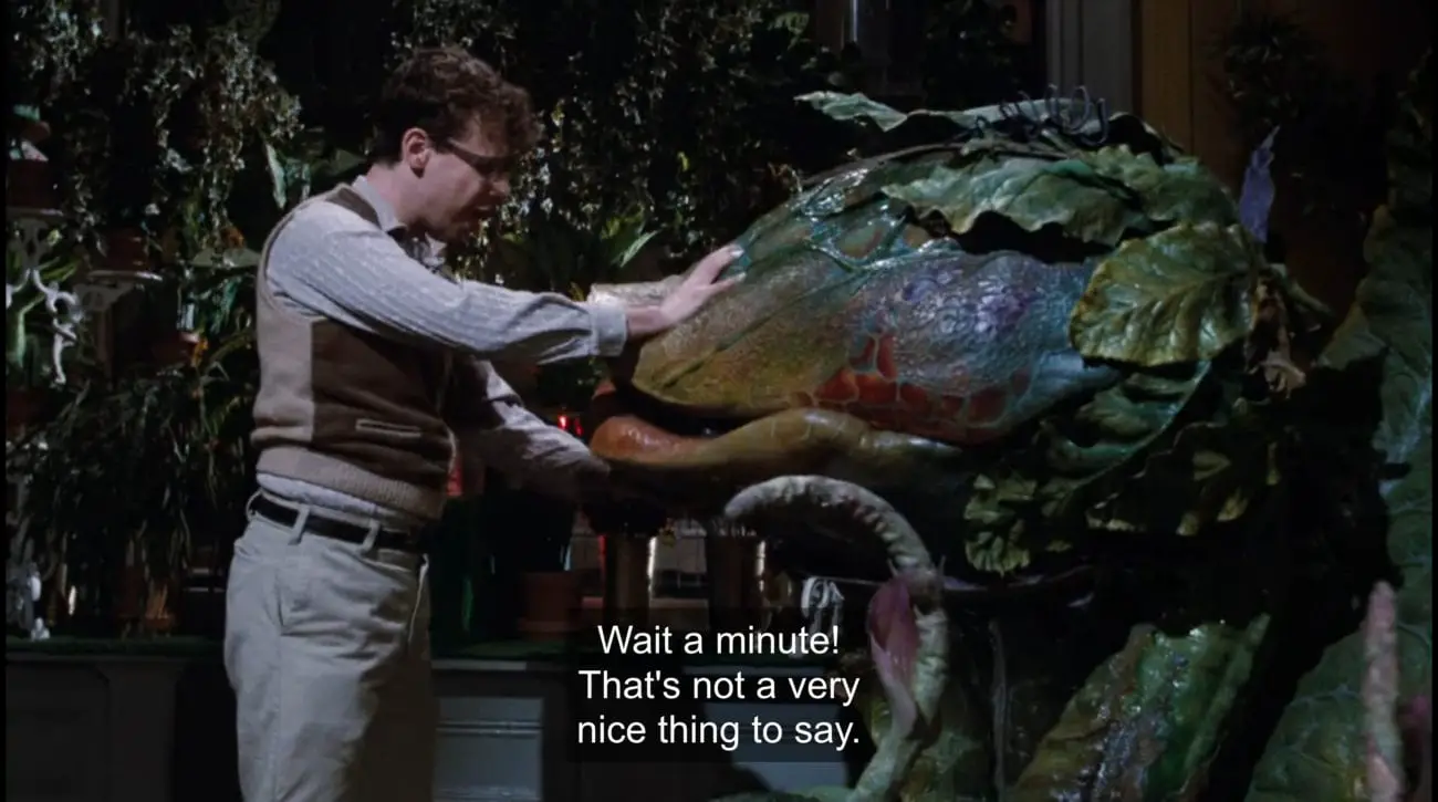 Seymour Krelborn (Rick Moranis) holds carnivorous plant Audrey II's (Levi Stubbs) mouth shut, yelling, "Wait a minute! That's not a very nice thing to say!", in the film, "Little Shop of Horrors" (1986).