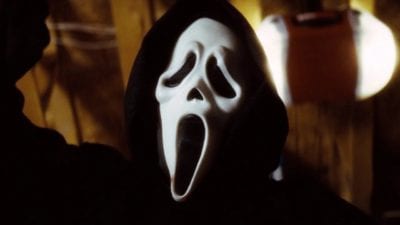 Close-up of hooded ghostface killer mask with arm raised holding a knife.