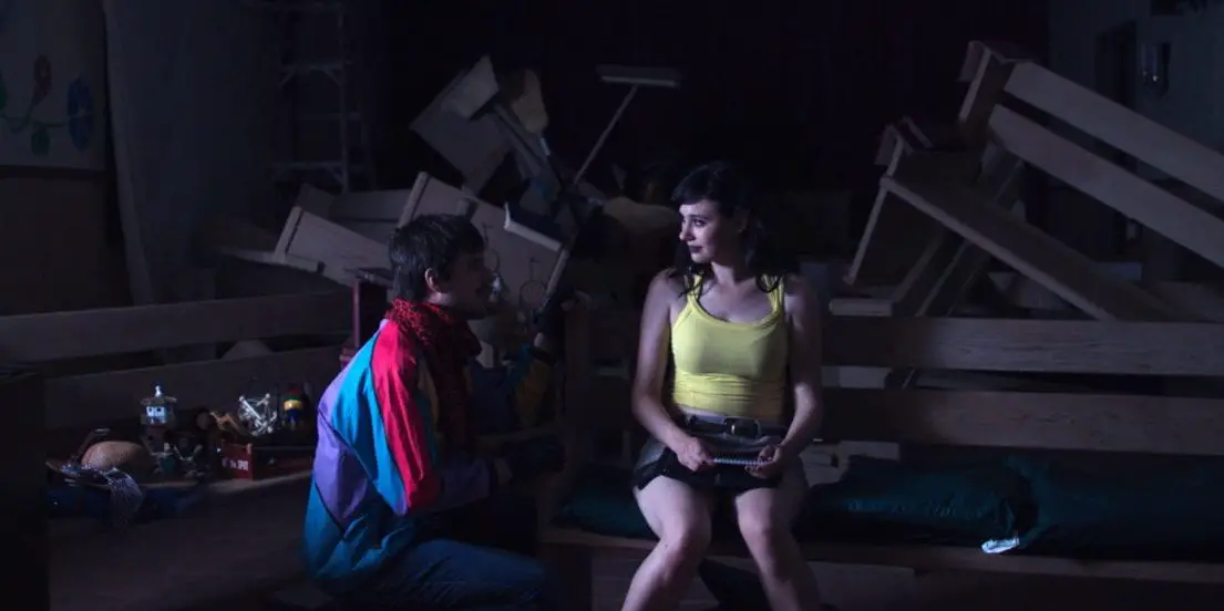 Remy, in a colorful jacket, and Danni, in a yellow tank top, talk in a church.