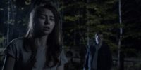 A night scene of a woman in the foreground and a man in the background in An Unquiet Grave