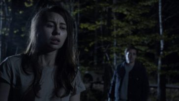 A night scene of a woman in the foreground and a man in the background in An Unquiet Grave