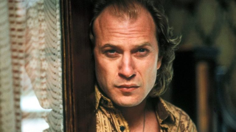 A scowling man leans against a door.