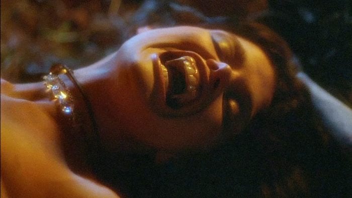 close-up of a woman's face as she opens her mouth in pleasure, showing a full set of elongated sharp teeth.