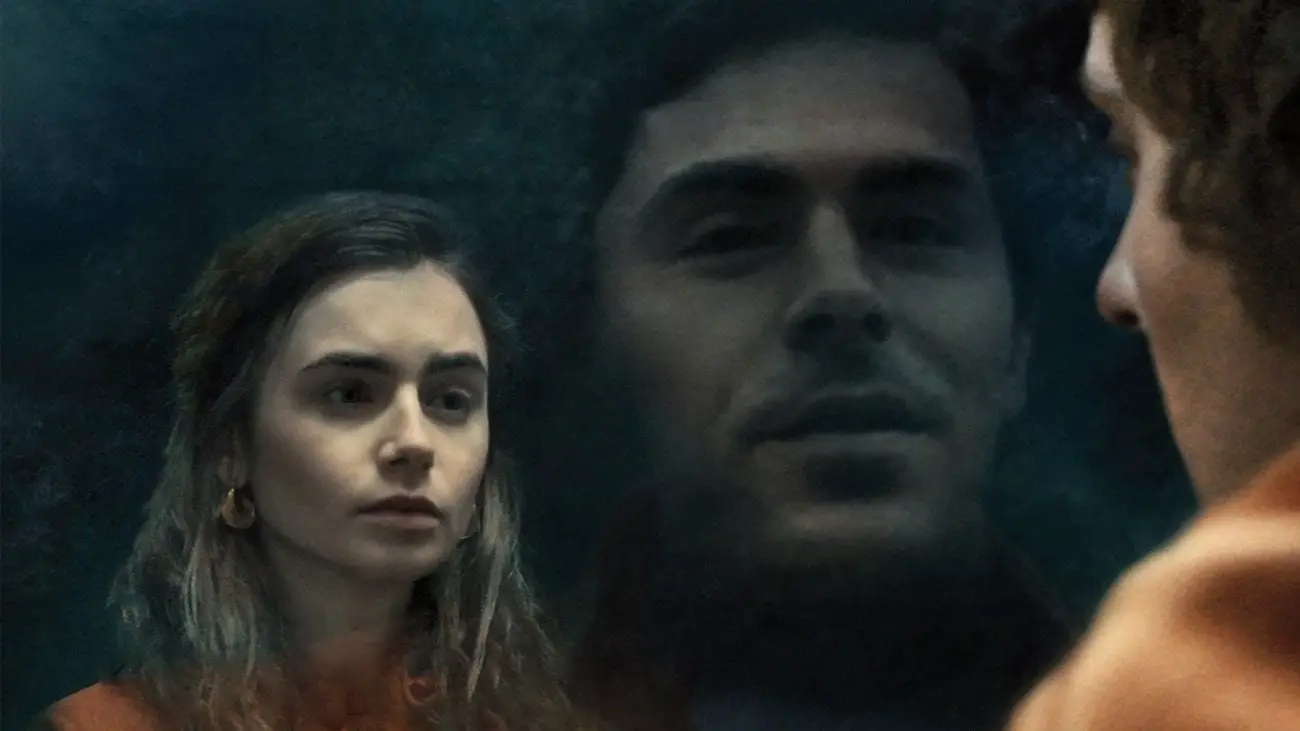 A man's face is reflected in glass. A woman looks back at him.