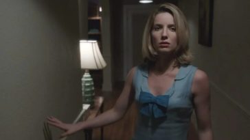 A woman in pajamas walks cautiously down a hallway.