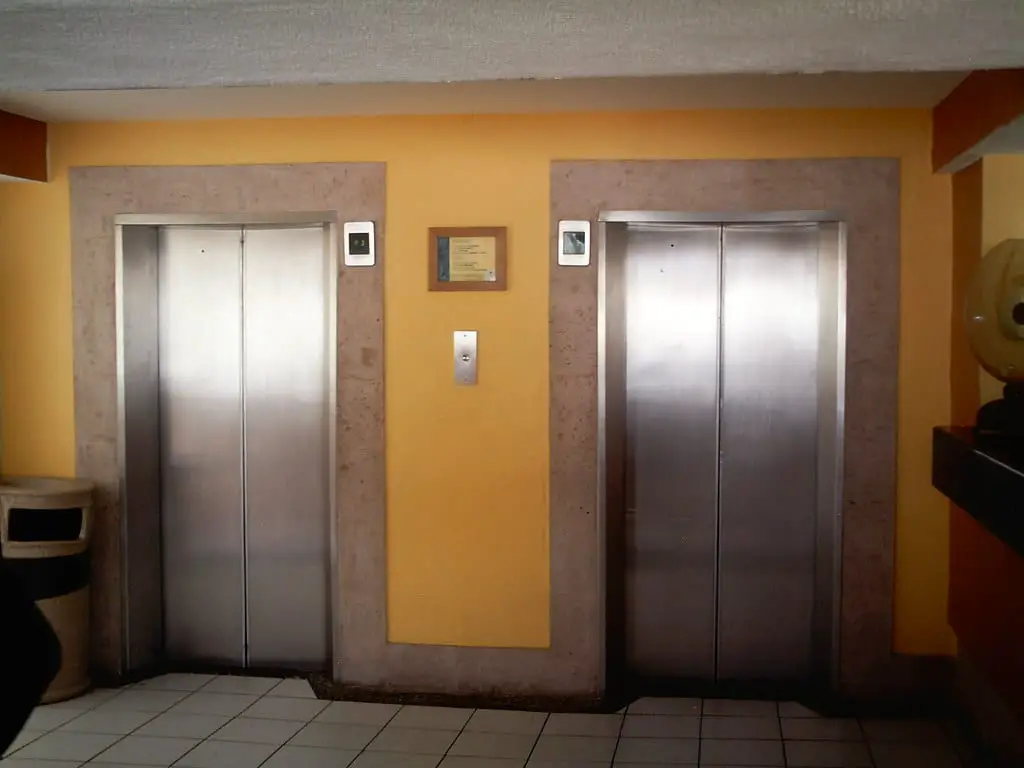 A shot of tow elevator doors, side by side, separated by a yellow wall.