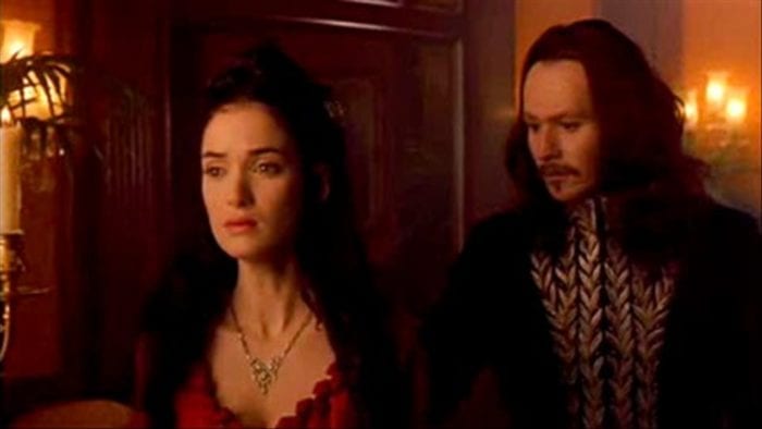 I woman stands with a look of sorrow as a man approaches from behind her with a concerned expression.