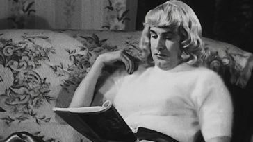 Ed Wood in the movie Glen Or Glenda, wearing an Angora sweater, blond wig, skirt and stockings as he sits on a couch.