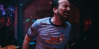 Nicolas Cage’s face contains a pained look as he winces toward the camera with a bloodied and ripped Willy’s Wonderland shirt on