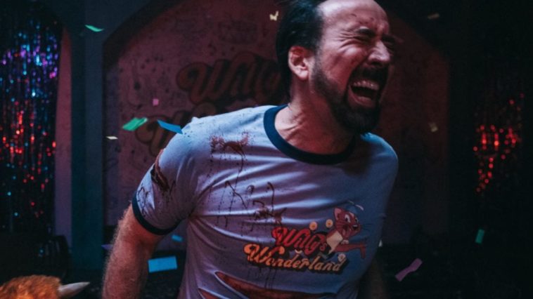 Nicolas Cage’s face contains a pained look as he winces toward the camera with a bloodied and ripped Willy’s Wonderland shirt on