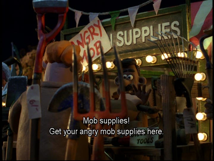 A male salesperson calls out, "Mob supplies! Get your angry mob supplies here!" from a stand that's labeled "Angry Mob Supplies," with the words "Angry Mob" on a sign stuck over the word "Garden," in the film, "Wallace & Gromit: The Curse of the Were-Rabbit" (2005).