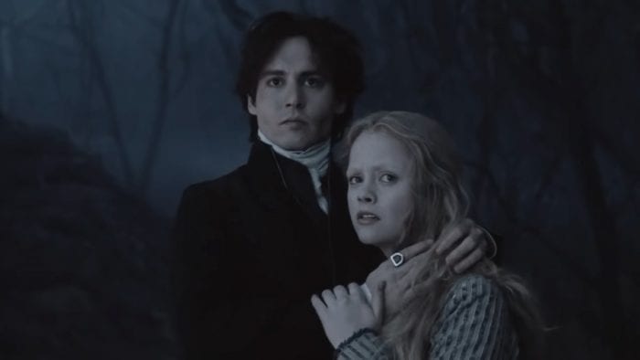A man stands and protectively puts his arms around a young woman as they both look at something on the distance.