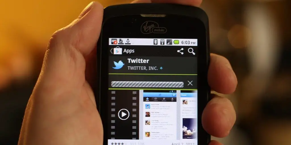 A hand holds a mobile phone with the Twitter app displayed on the screen.
