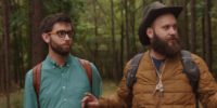 Brian and Jeff hear a sound as they walk through the woods, Jeff puts up his index finger on his right hand instructing Jeff to be still as they both look to their left into the woods.