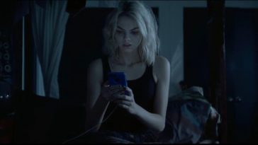 Cadence sits in her bed holding her phone with both hands and staring at it nervously