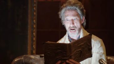 A man opens the Necronomicon and a light shines up from the book as the man stares on with a shocked look on his face