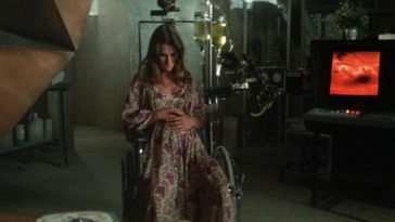 A pregant woman sits, holding her stomach in a dark, dingy room.