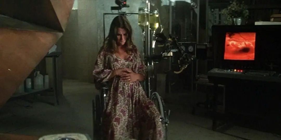 A pregant woman sits, holding her stomach in a dark, dingy room.