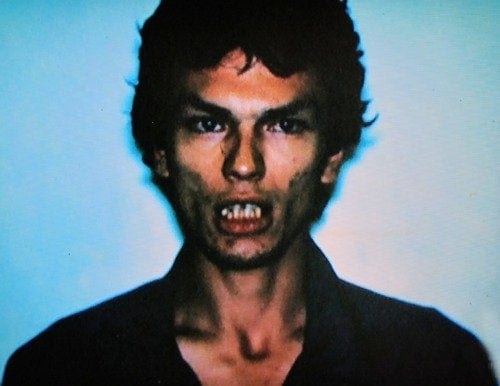 A color picture of Richard showing his poor teeth. His mouth is open, but he isn;t smiling. He is standing near a blue wall wearing a black shirt. 