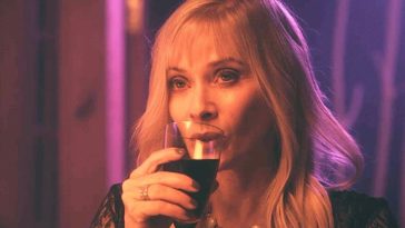 A blonde woman sips a drink out of a glass.