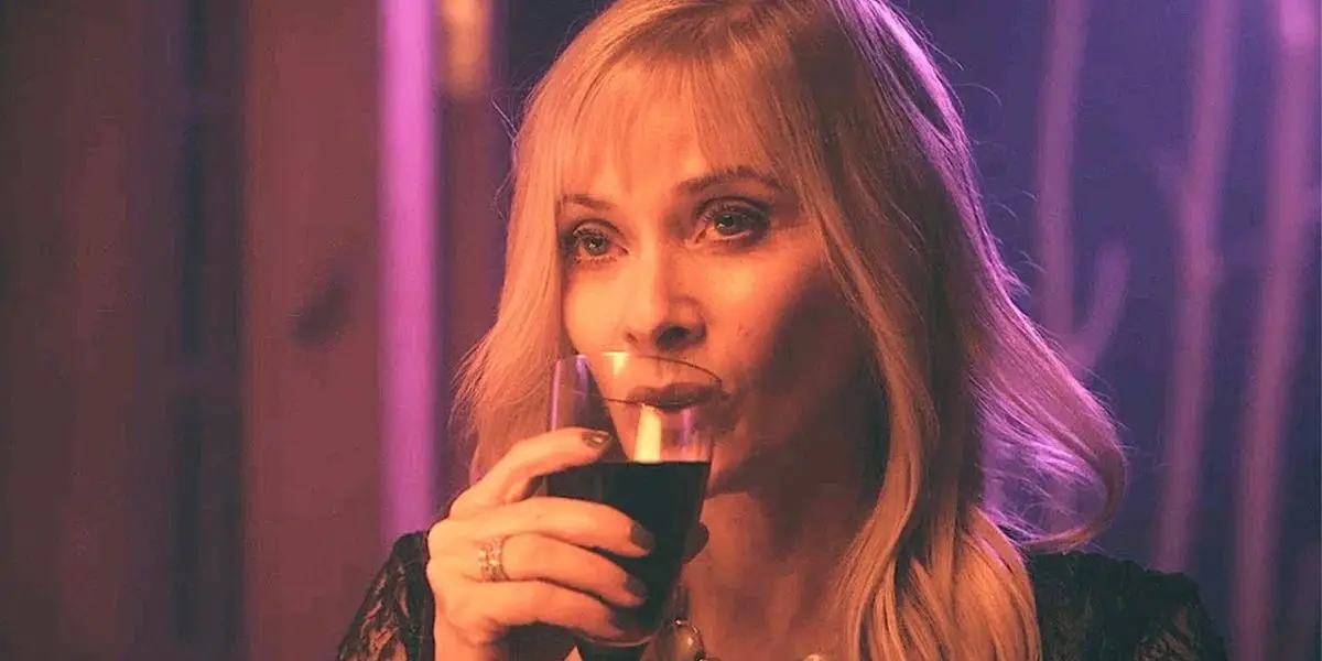 A blonde woman sips a drink out of a glass.
