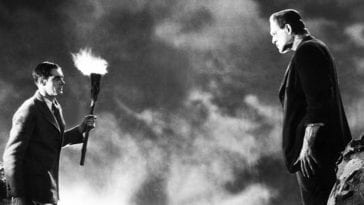 Dr. Frankenstein holds a torch and stands defiantly across from the monster