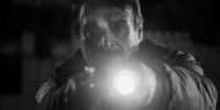 A night watchman points his flashlight and gun at the camera with a shocked look on his face