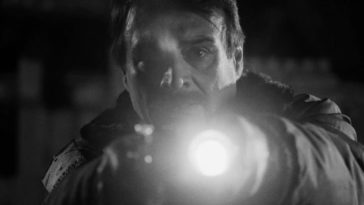 A night watchman points his flashlight and gun at the camera with a shocked look on his face